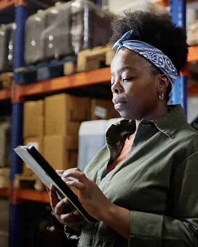 Eine Frau steht in einem Warenlager und kontrolliert den Zustand eines Lagers, als einen Teil der Zertifizierung. Sie führt ein Audit durch.